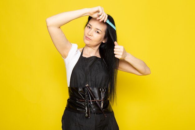 Free photo a front view beautiful female hairdresser in white t-shirt black cape with brushes with washed hair brushing her hair posing on the yellow background stylist barber hair