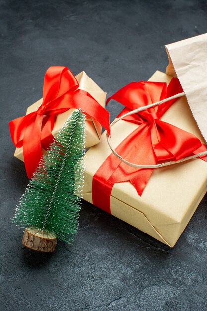 Front view of beautiful gifts with red ribbon and christmas tree on a dark table