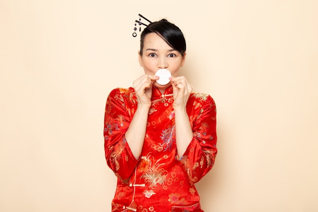 A front view beautiful japanese geisha in traditional red japanese dress with hair sticks posing holding little white cotton expression on the cream background ceremony japan