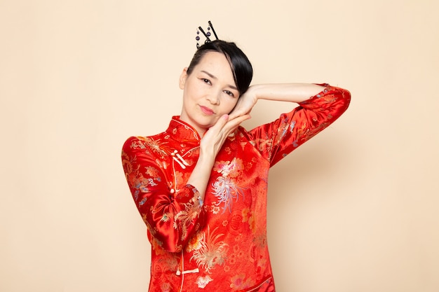 A front view beautiful japanese geisha in traditional red japanese dress with hair sticks posing with her hands on the cream background ceremony entertaining japan east