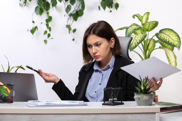 A front view beautiful young businesswoman in black jacket and blue shirt working with laptop in front of table business job office