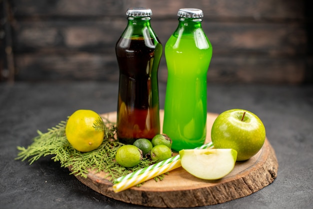 Front view black and green juices in bottles apple lemon feijoas pipettes on wood board