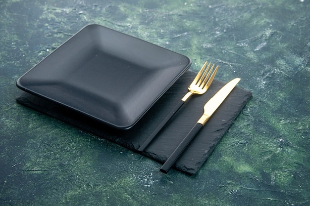 front view black square plate with golden fork and knife on dark background