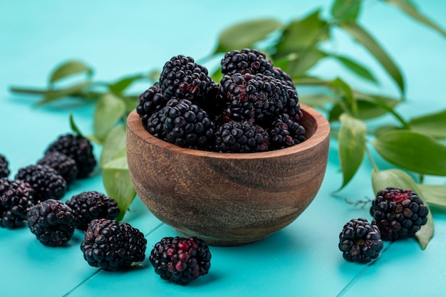 Front view of blackberry in a wooden bowl on a light blue surface