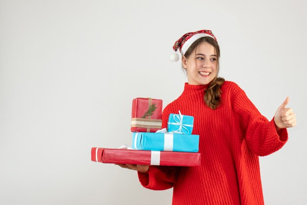 Front view blissful girl with santa hat making thumb up sign holding her xmas gift