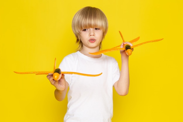 Free photo front view blonde boy holding toy orange planes on the yellow desk