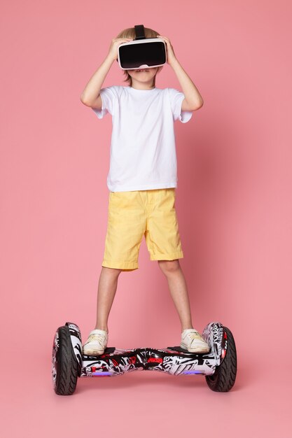 A front view blonde boy in white t-shirt playing vr riding segway on the pink space