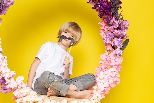 Free Photo a front view blonde funny boy in white t-shirt holding mustache on the yellow floor