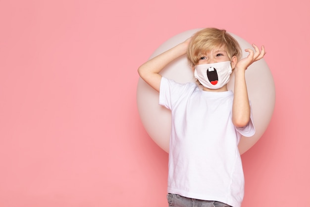 Free photo a front view blonde smiling boy in white t-shirt and funny mask on the pink space