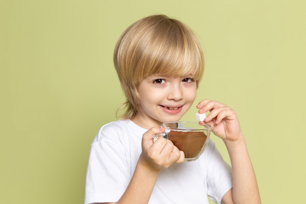 Free photo a front view blonde smiling child in white t-shirt holding powdered coffee on the stone colored desk