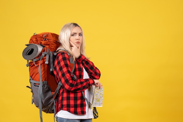 Free photo front view blonde traveler woman with her backpack holding map putting hand on her chin standing on yellow wall