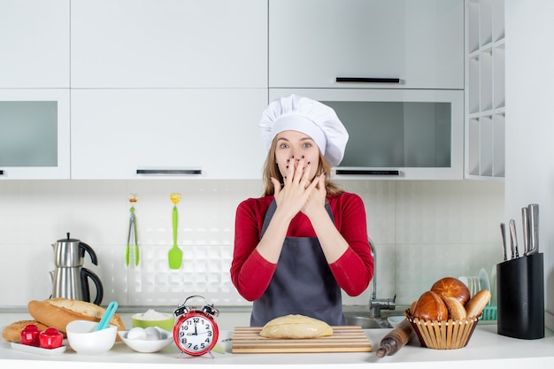 Front view blonde woman in cook hat and apron putting hands on her face in the kitchen