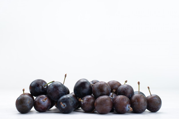 Front view of blue plums round formed on the white surface