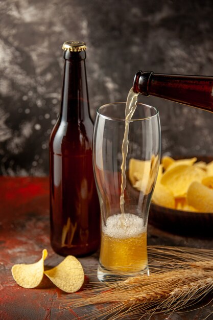 Front view bottle of bear pouring up into the glass with cips on the dark background