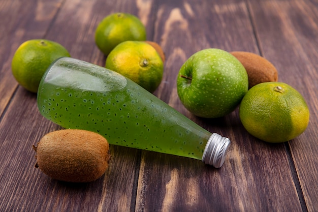 Front view bottle with juice with tangerines kiwi and apple on wooden wall