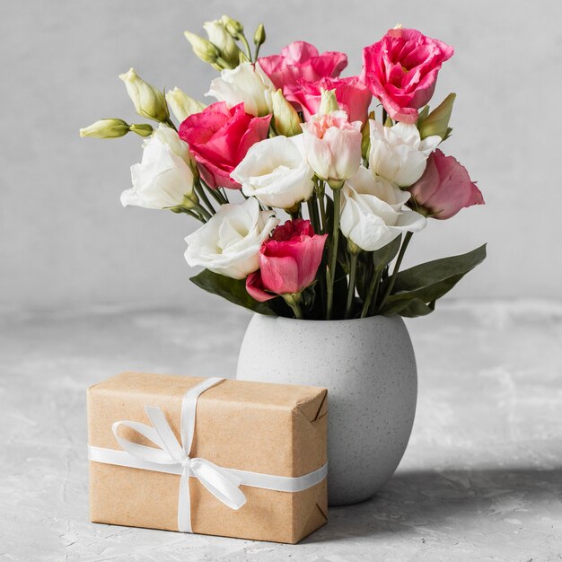 Front view bouquet of roses in a vase next to a wrapped gift