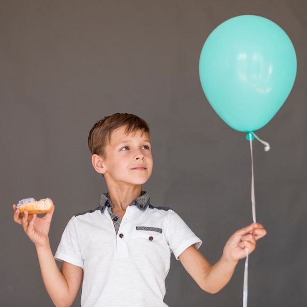 Free Photo front view boy holding a balloon and a doughnut