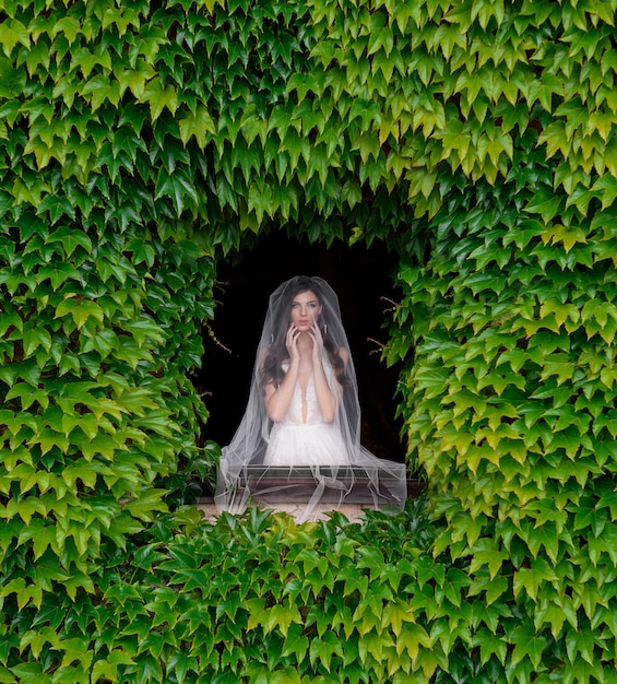 Front view of bride standing before the window with fresh greenery frame