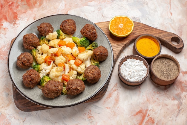 Free photo front view broccoli and cauliflower salad and meatball on plate on cutting board different spices in small bowls on nude isolated background