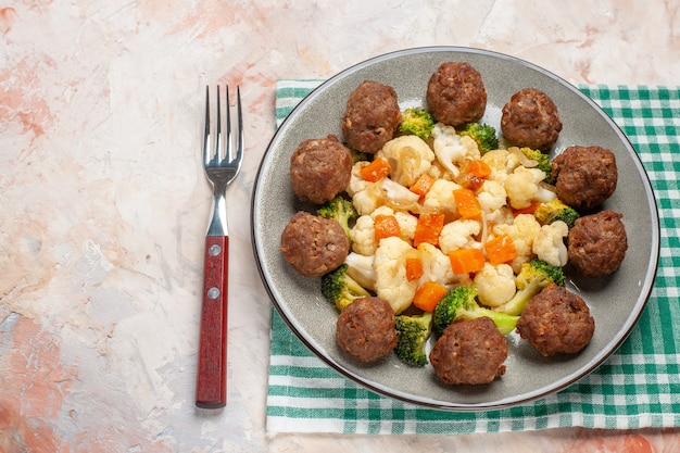 Free photo front view broccoli and cauliflower salad and meatball on plate green and white checkered napkin a fork on nude isolated background