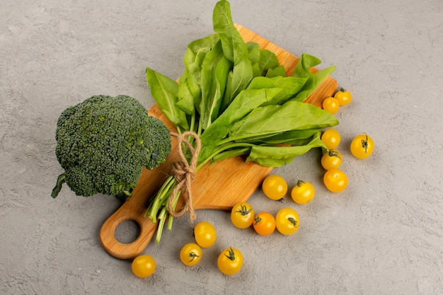 front view broccoli green leafs along with yellow tomatoes on the grey background