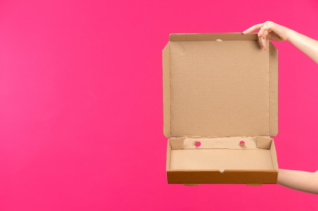 Free photo a front view brown empty package hand holding empty package female hand pink background color food