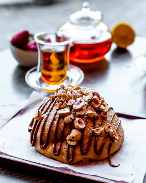 Front view bun with nuts and armouda glass of tea with lemon and a teapot of tea on the table