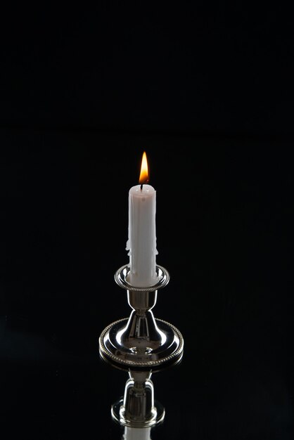 Front view of burning candle in golden stand on dark surface