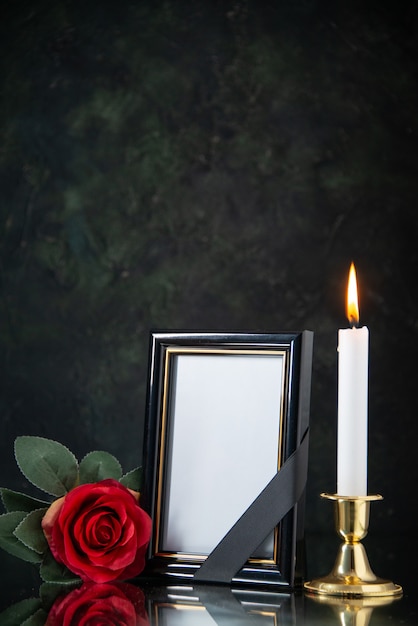 Front view of burning candle with red flower on black surface