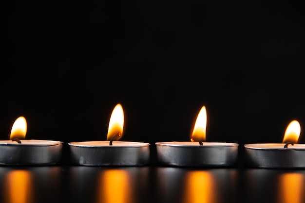 Front view of burning candles on a dark surface