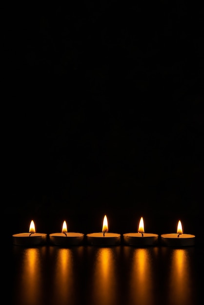 Front view of burning candles on the pitch black surface