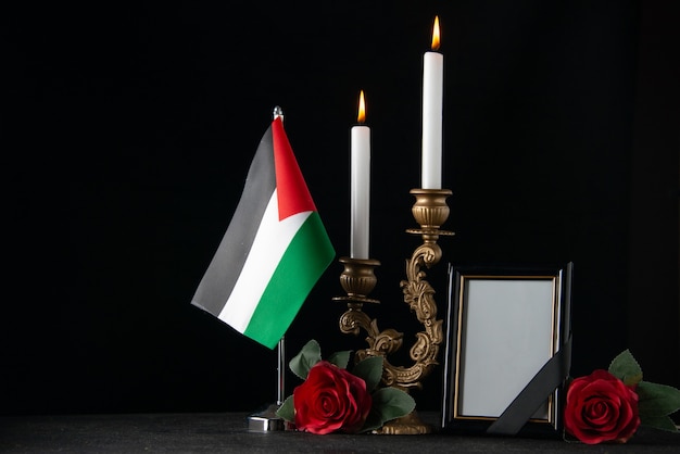 Front view burning candles with palestinian flag and picture frame dark surface