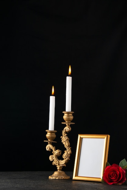 Front view of burning candles with picture frame as memory on a dark surface