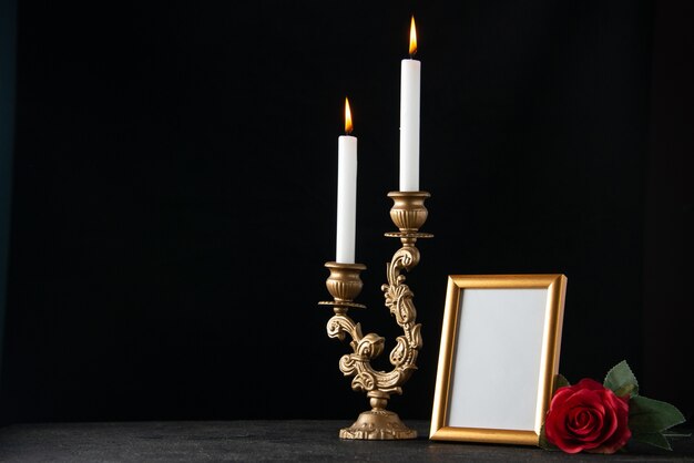 Front view of burning candles with picture frame on dark surface