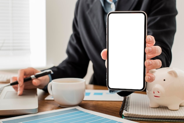 Front view of businessman at the office holding blank smartphone