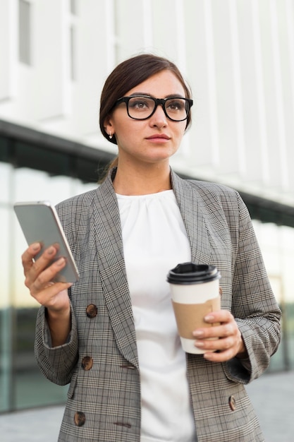 Front view of businesswoman with coffee and smartphone outdoors