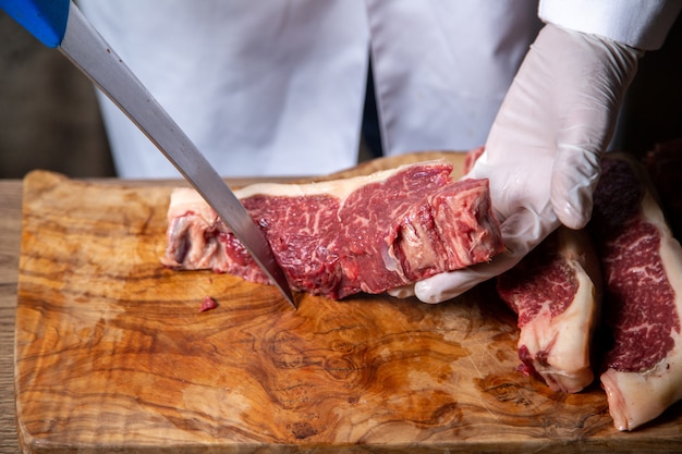 Front view of butcher cutting meat in white gloves holding big knife on the wooden desk