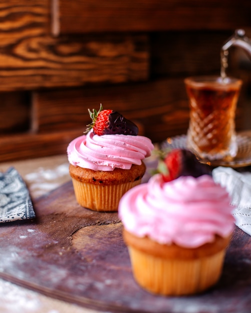 Front view cakes with pink cream and strawberry along with hot tea on the brown surface