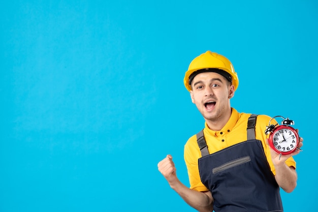 Front view cheering male worker in yellow uniform with clocks on blue 