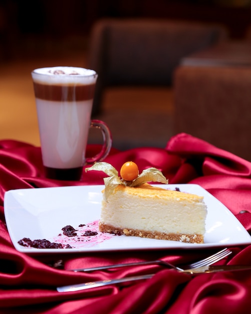 Free photo front view cheesecake decorated with a berry on a plate and with a cup of late