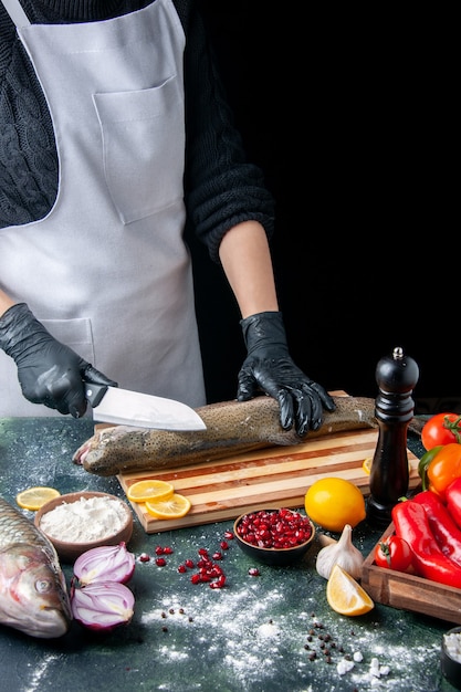 Front view of chef in apron chopping raw fish on wood board pepper grinder flour bowl pomegranate seeds in bowl on kitchen table