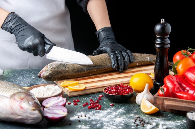 Front view chef chopping raw fish on wooden board pepper grinder flour bowl pomegranate seeds in bowl on kitchen table