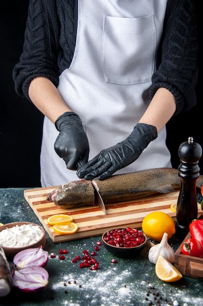 Front view chef cutting head of fish on chopping board pepper grinder flour bowl pomegranate seeds in bowl on kitchen table