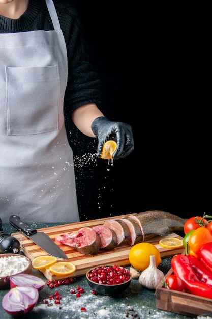 Front view chef squeezing lemon on fish slices knife on cutting board vegetables on wood serving board on kitchen table