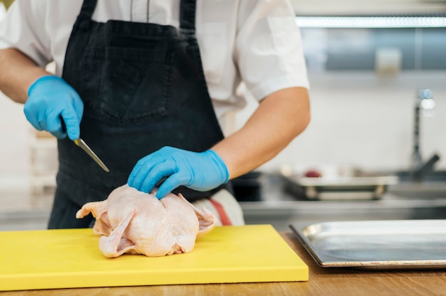 Free photo front view of chef with gloves cutting chicken