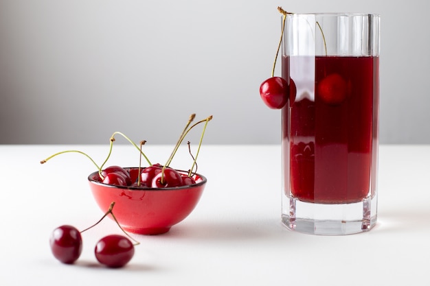 Free photo front view of cherry juice inside long glass with fresh cherries on the white surface