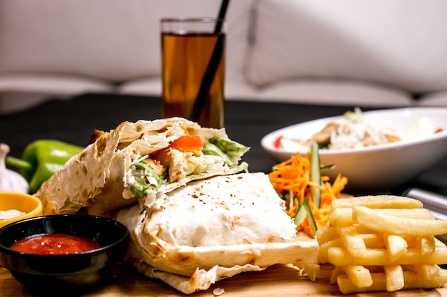 Front view chicken doner in pita bread with ketchup mayonnaise french fries and vegetable salad on the board