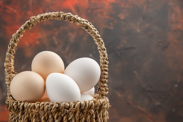 Front view chicken eggs inside basket on the dark surface