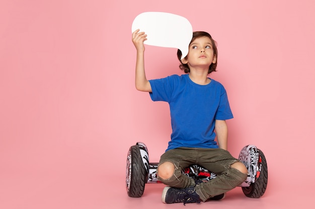 A front view child boy adorable sweet in blue t-shirt sitting on the segway on the pink floor