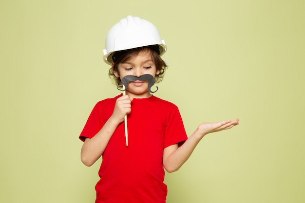 Free photo a front view child boy adorable sweet holding mustache in red t-shirt and white helmet on the stone colored space